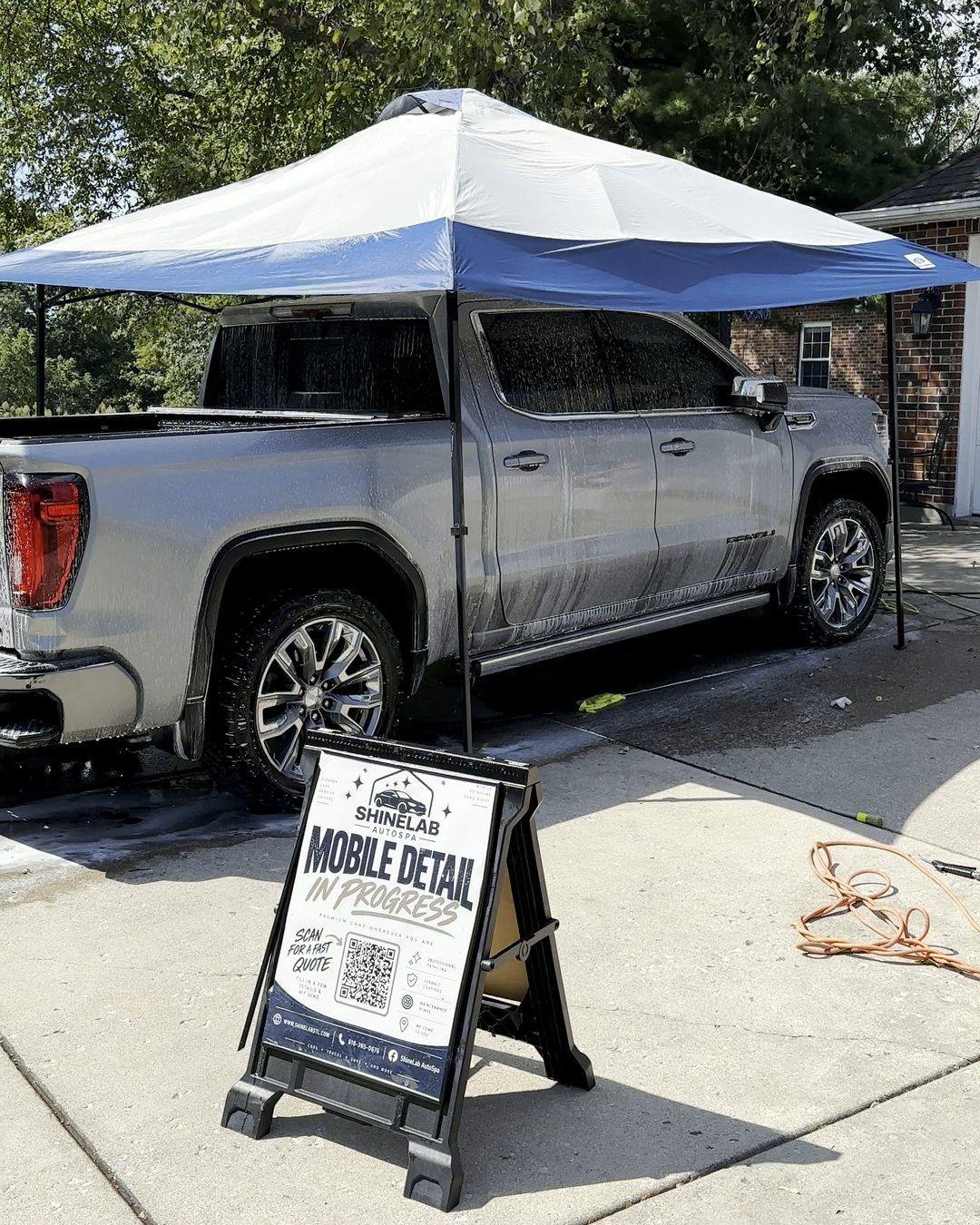 ShineLab canopy and Mobile Detail in Progress sign set up beside a silver GMC Sierra in a customer's driveway